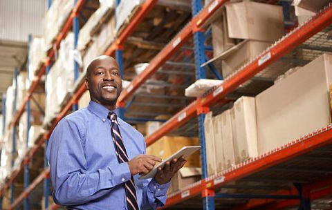 Businessman With Digital Tablet In Warehouse Looking At Camera Smiling